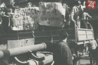 Demonštranti na korbe nákladného auta s ručne vyrobenými plagátmi bránia prechodu tanku.